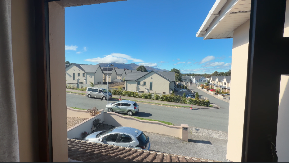 View out of a window of a neighborhood in Killarney with a view of mountains above the homes.