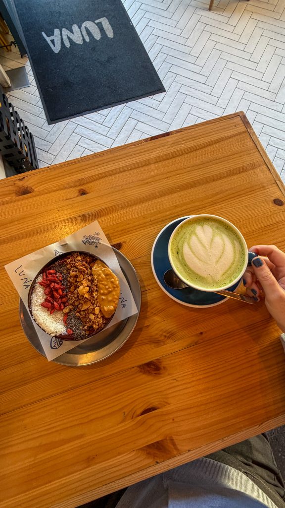 Wood table with an acai bowl and matcha latte sitting on it.