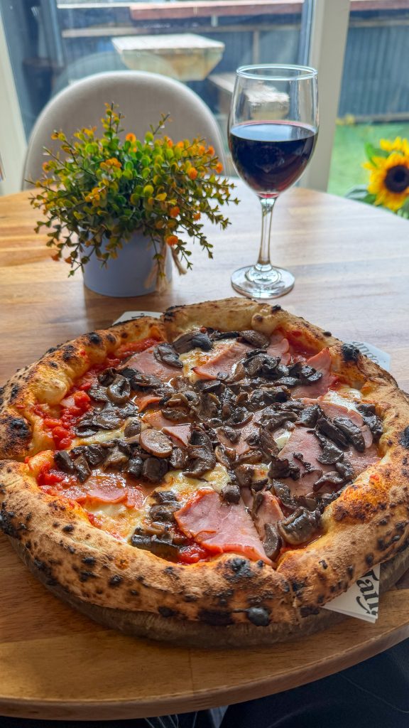 Meat pizza sitting on a table with a glass of red wine.