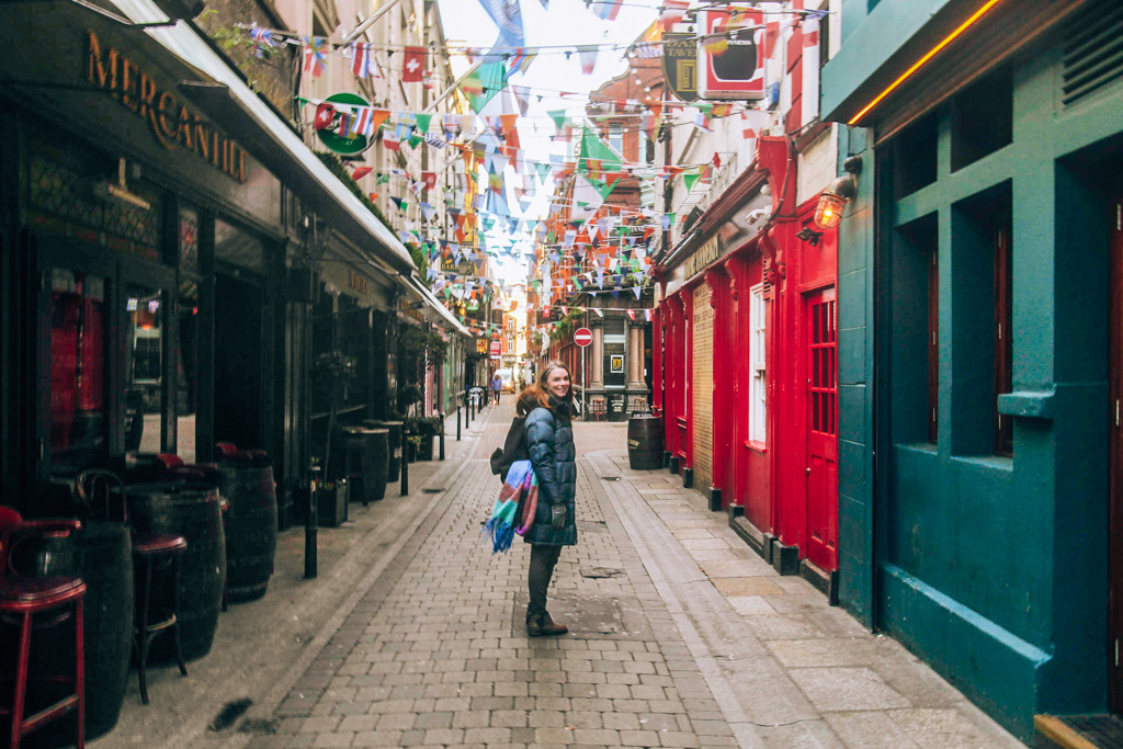 Katie standing on a colorful street in Dublin with flags hanging between the historic buildings.