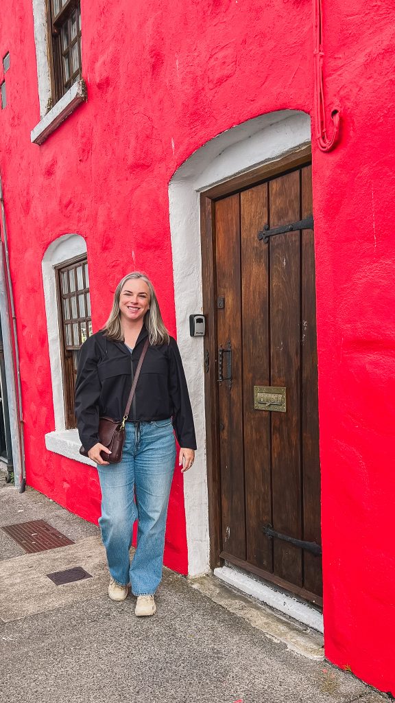 Katie standing in front of a bright red house along the Long Walk in Galway.