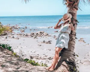 Me leaning on a tree with a hat over my face on the beach.