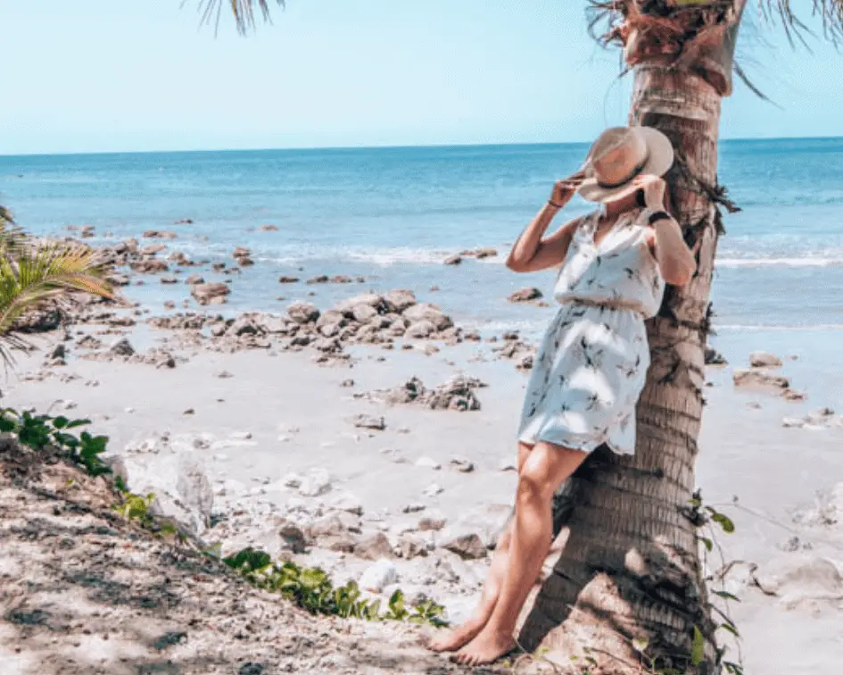 Me leaning on a tree with a hat over my face on the beach.