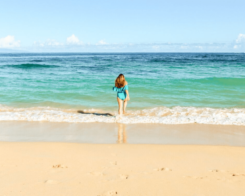 Baldwin Beach: One of the Best Beaches in Paia Maui. Woman wearing a teal swimsuit walking into the turquoise blue Pacific Ocean inMaui.