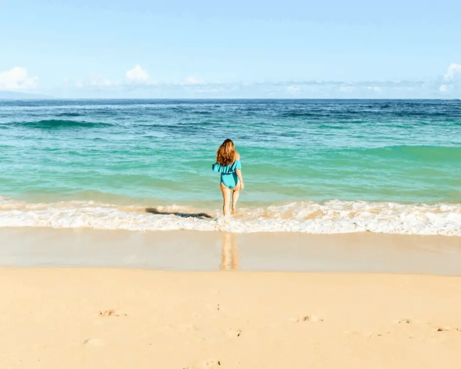 Baldwin Beach: One of the Best Beaches in Paia Maui. Woman wearing a teal swimsuit walking into the turquoise blue Pacific Ocean inMaui.