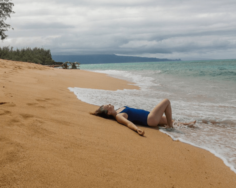 Me laying on Secret Beach in Paia Maui in a blue one piece swimsuit.