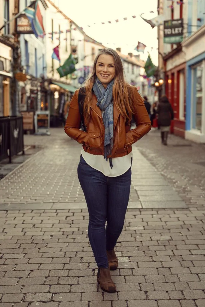 Woman walking down cobblestone street facing the camera.