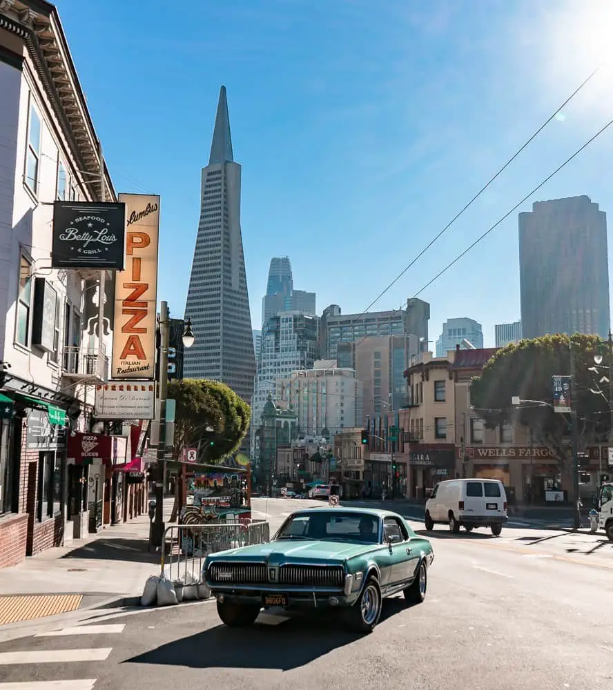 Car driving on a street in North Beach with the Transamerica building in the background.