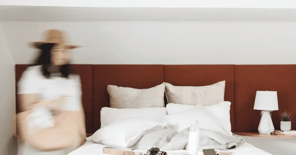Book one night of accommodation when planning a solo trip. Image of a woman walking towards a hotel bed.