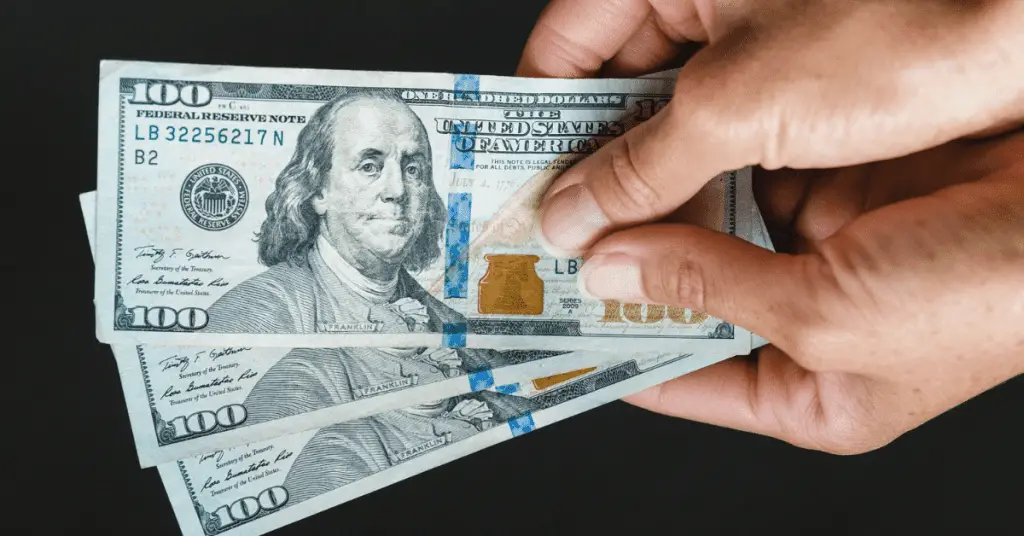 Need to plan a budget friendly solo trip? Here are a few tips! Image of hands holding 3 $100 bills.