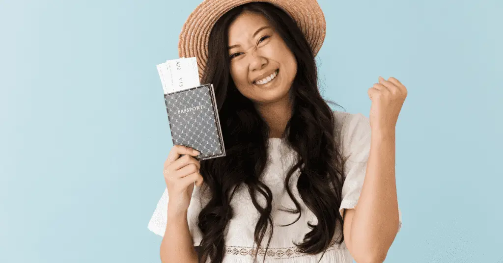 How to plan a solo trip? Make sure you get your Passport and other paperwork in order early. Image of a woman holding a passport and smiiling.