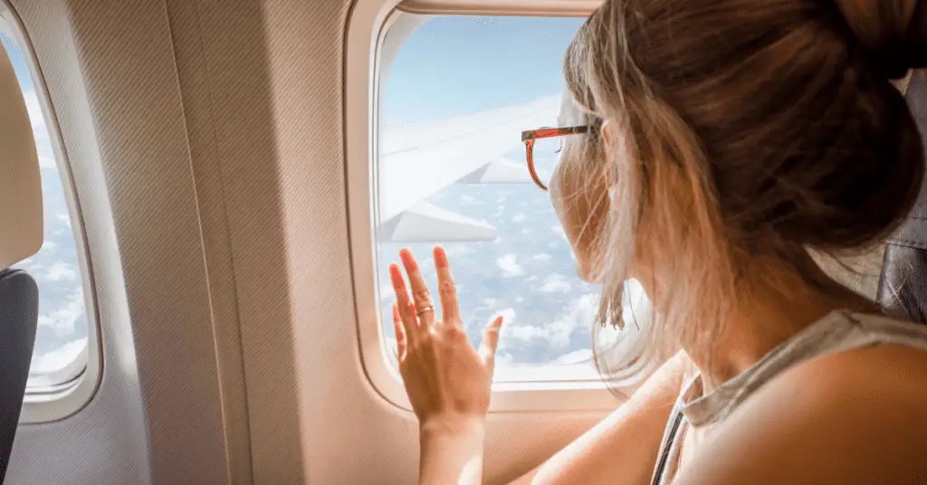 Planning a solo trip? Make sure to book your transportation using these steps! Image of a woman looking out of an airplane window.