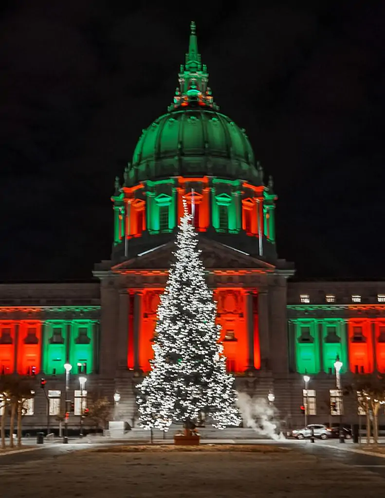 City Hall lit up in red and green with a Christmas tree in front for Christmas in San Francisco.