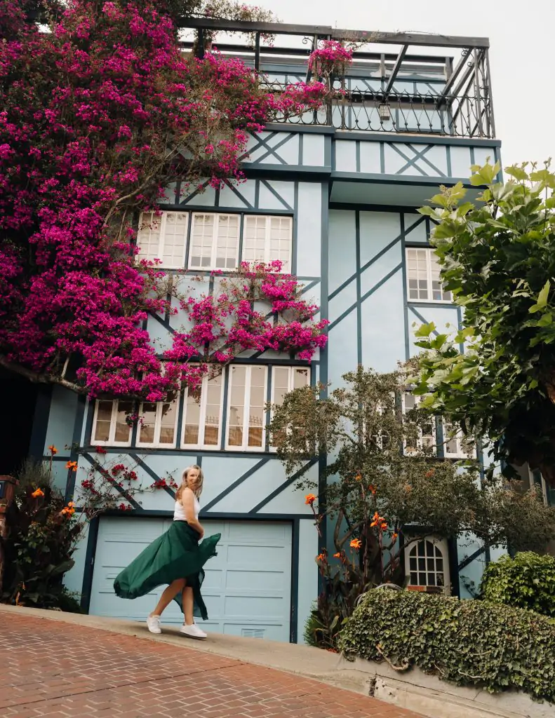 Me twirling in a dress in front of a blue house with pink flowers for a San Francisco photo opportunity.