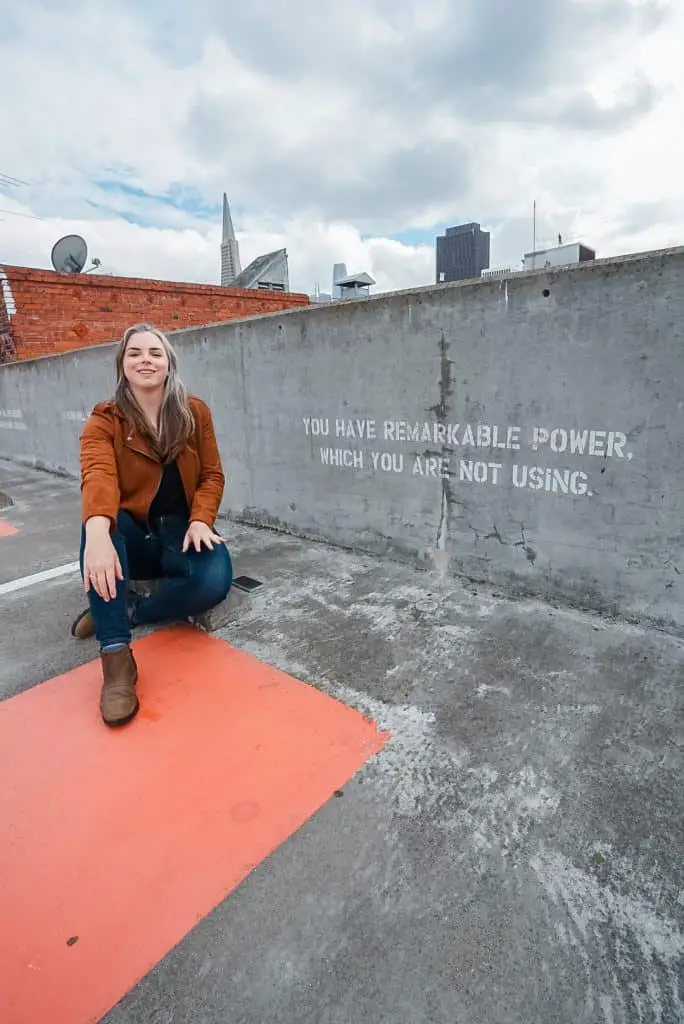 Me sitting on the ground of the top floor of the North Beach parking garage with a fortune painted on the wall.