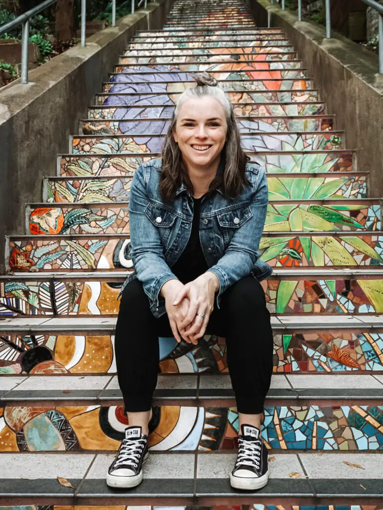 Me sitting on the Hidden Garden tiled stairs in San Francisco wearing a jean jacket and black jumpsuit.