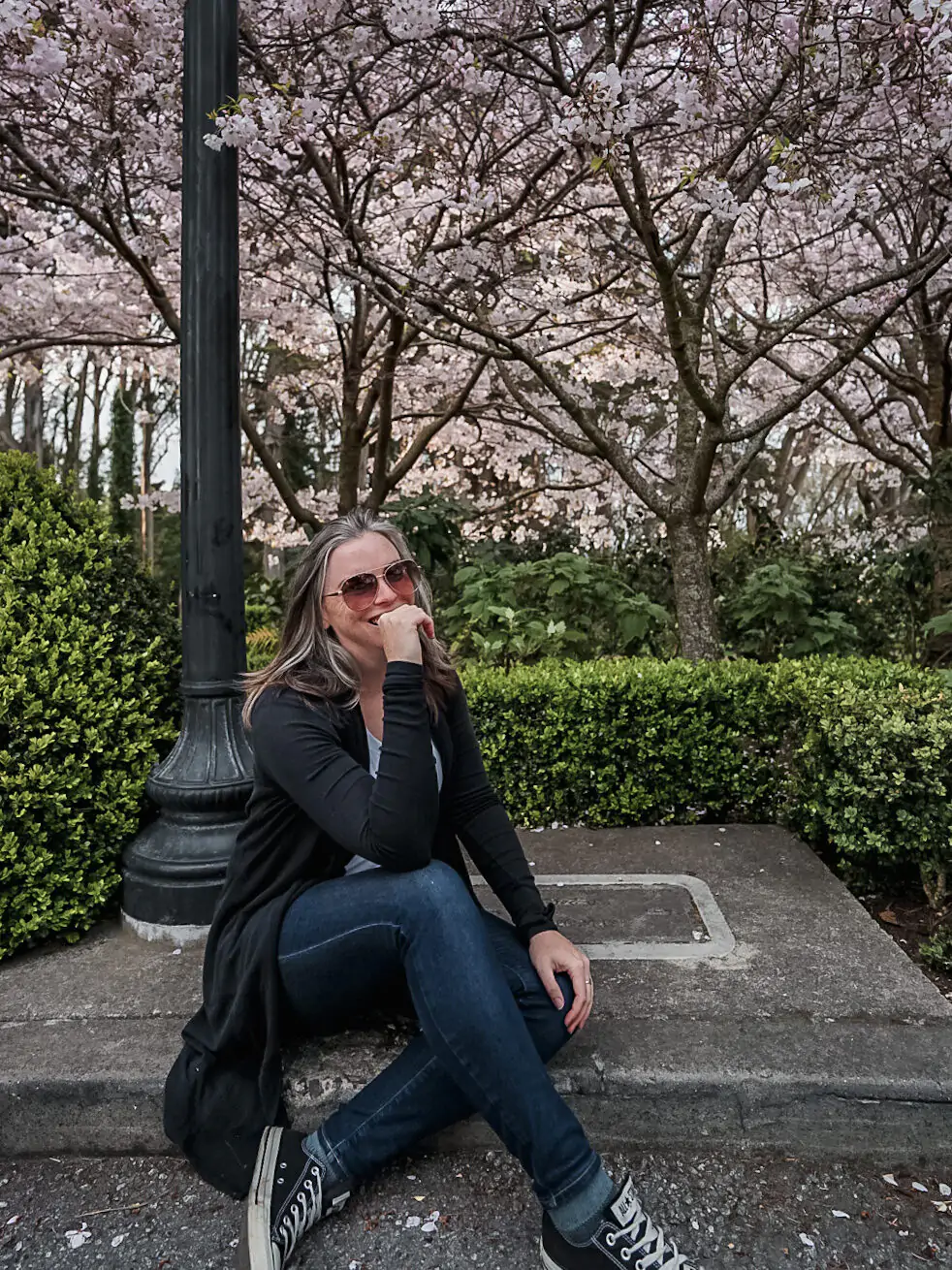 Me sitting on the ground wearing jeans and a long black sweater underneath Cherry Blossom trees during Spring in San Francisco.