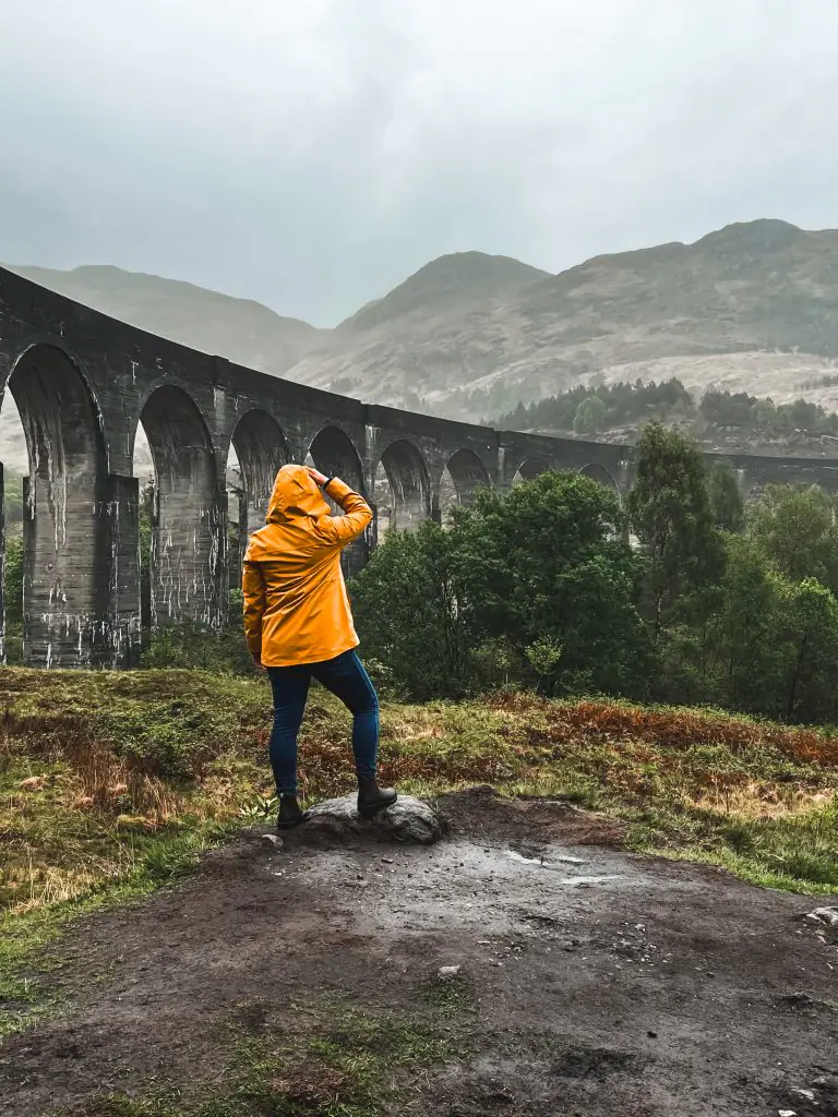 Me wearing a yellow rain jacket while looking at the Glenfinnan viaduct.