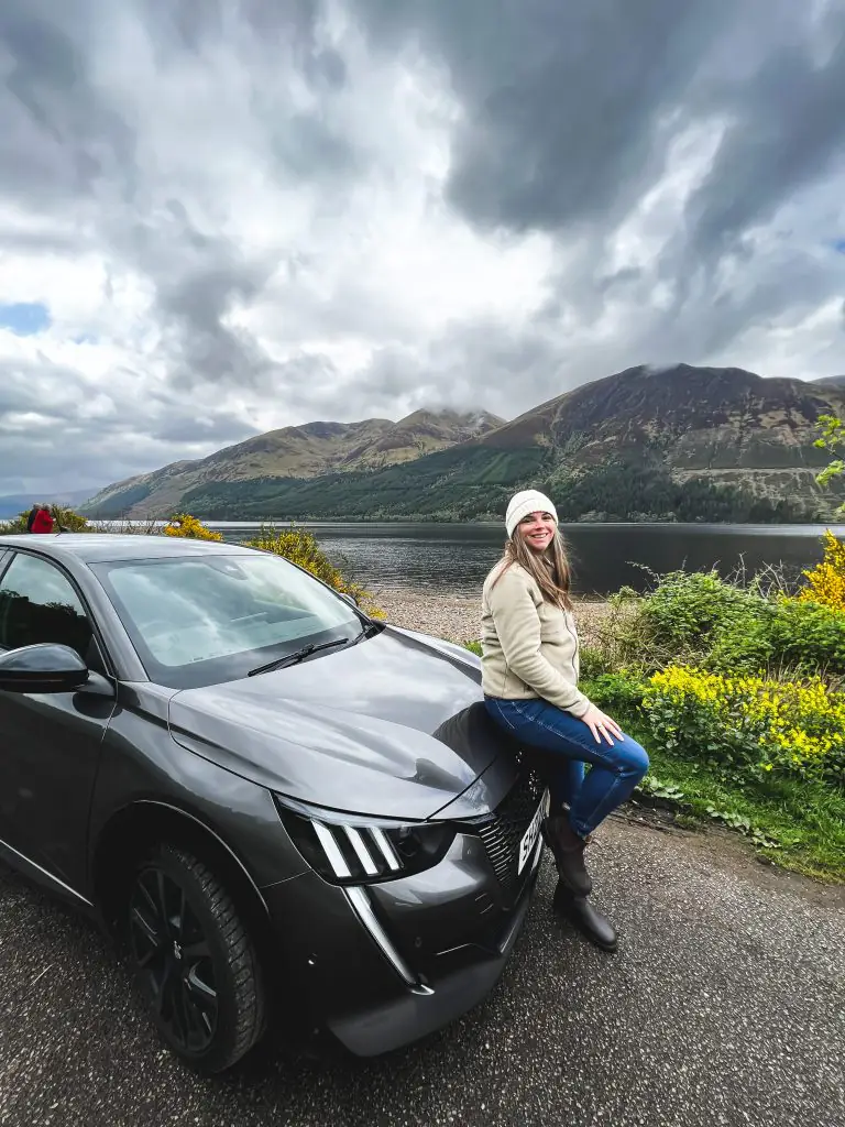 Me leaning up against my car in front of a lake during my Scotland road trip.