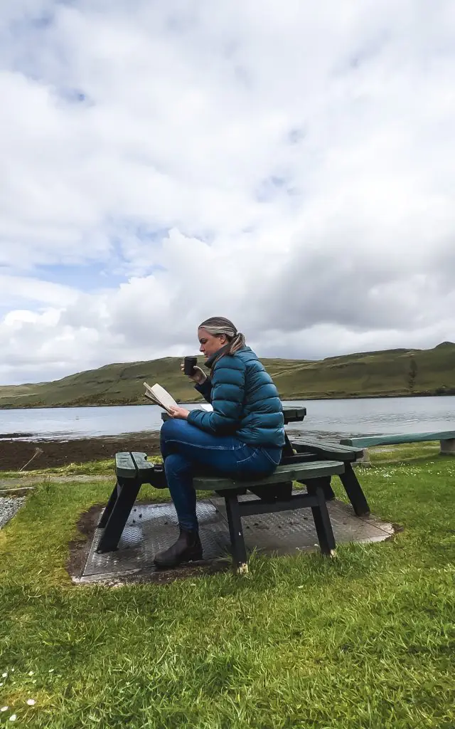 Me sitting on a bench in Scotland reading a book and sipping tea.