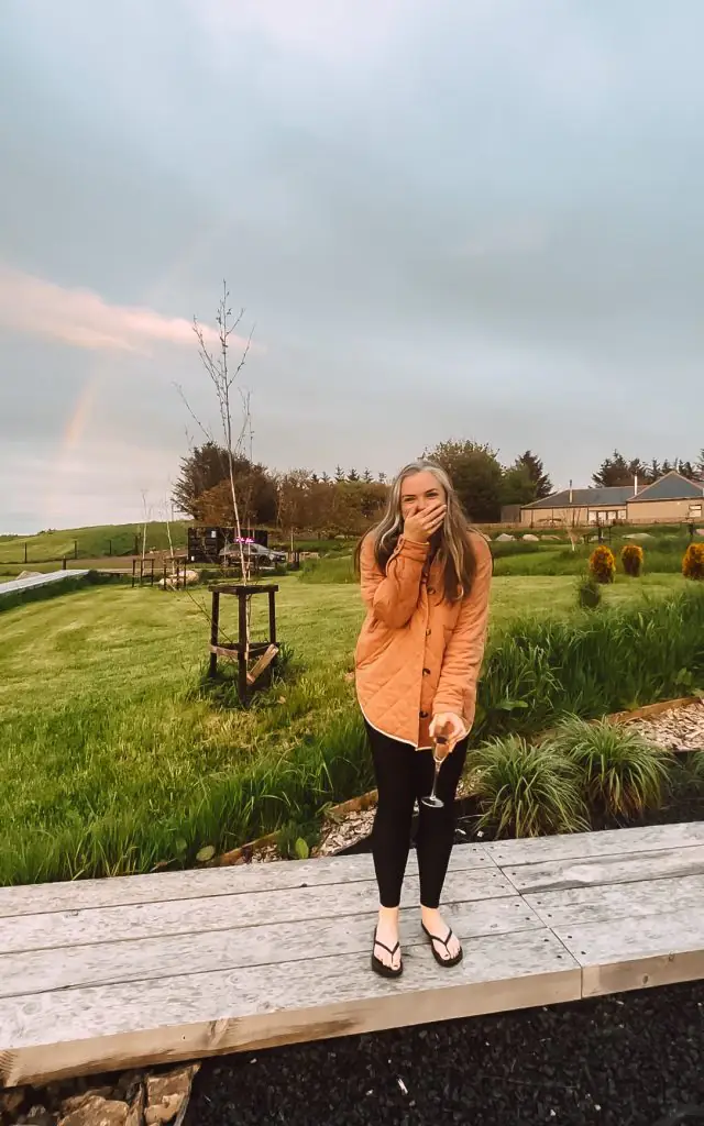 Me smiling in a Scotland field with a rainbow in the sky.