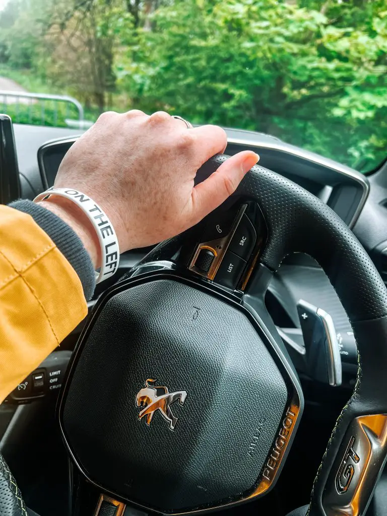 Hand on steering wheel of car. Scotland road trip itinerary.