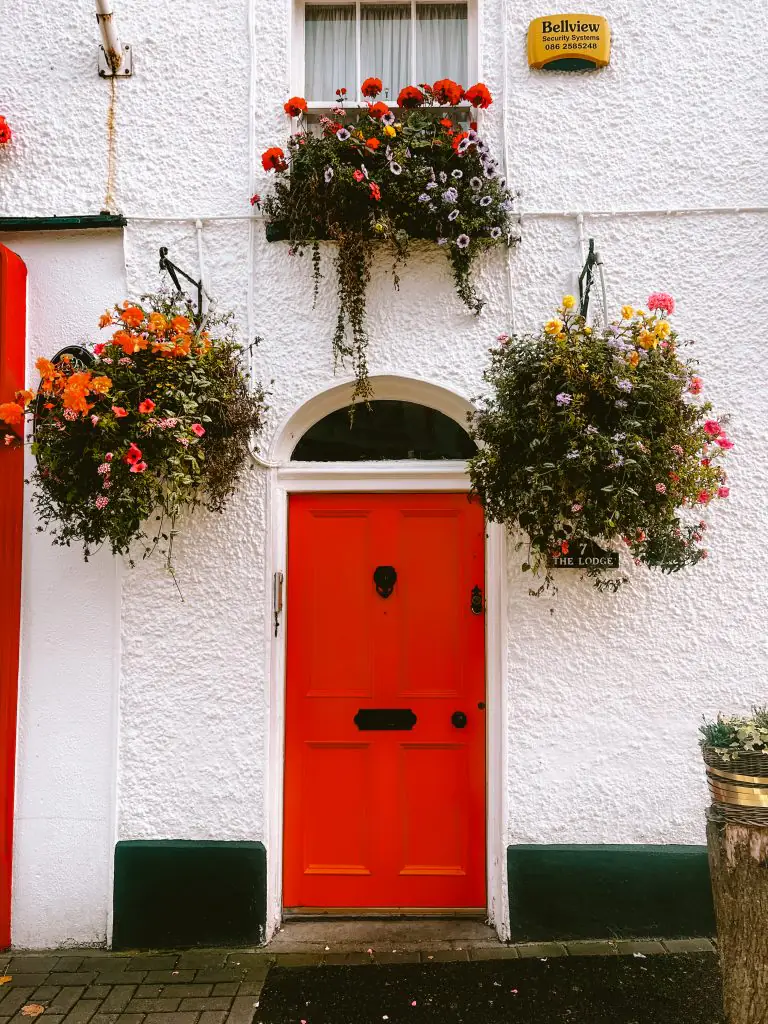 Orange door of a white building with hanging planters.