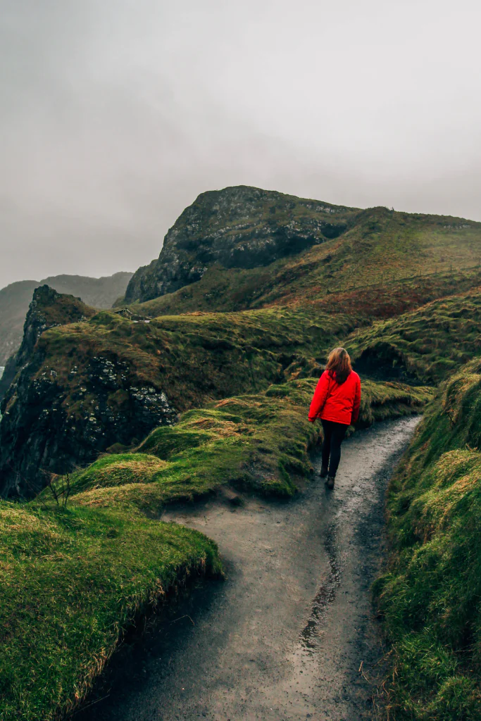 Woman in a red jacket walking through green hills.