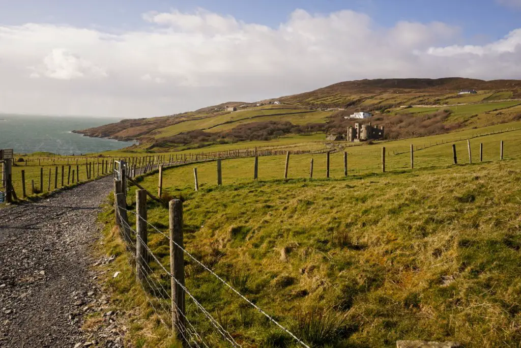 Gravel path and green landscape with the sea and a castle in the distance.