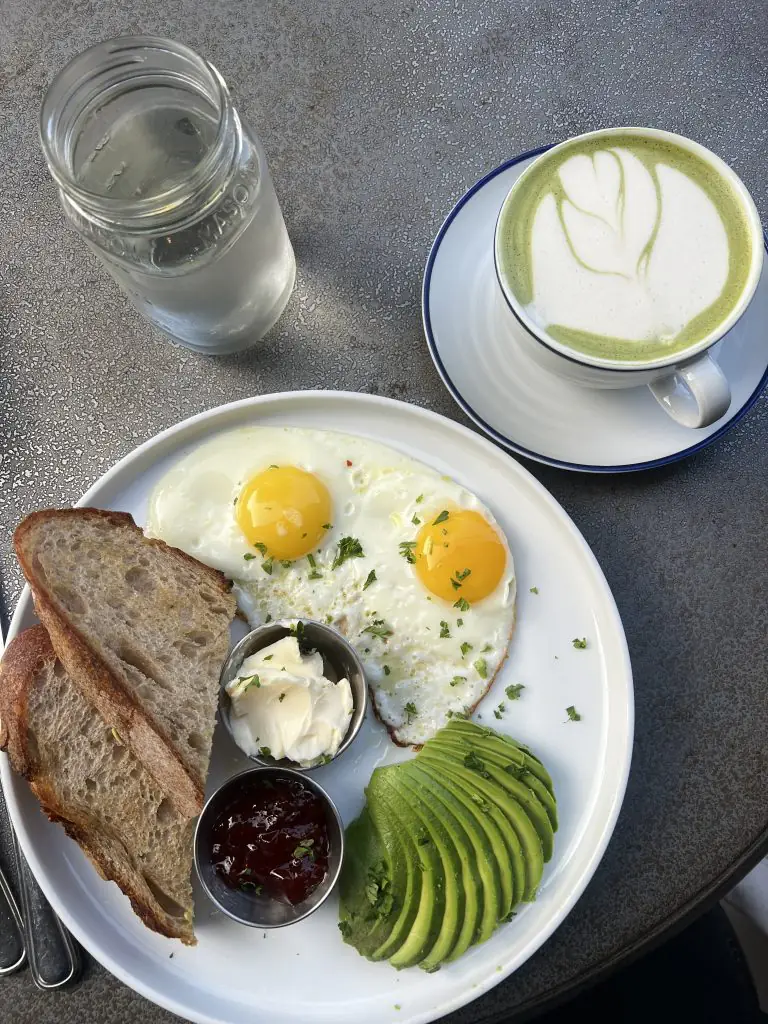 Breakfast of eggs, toast, and avocado with a matcha latte.