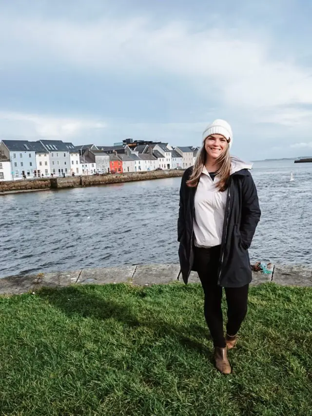 standing on a grassy patch in front of Galway Bay and the colorful houses.