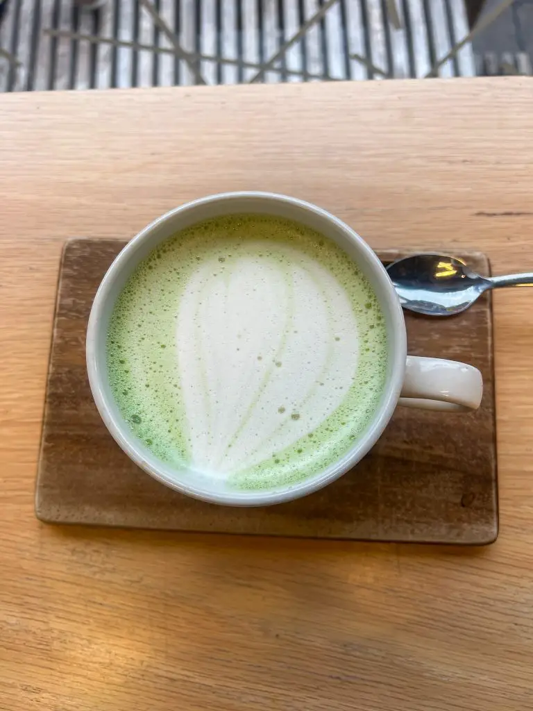 Green matcha latte in a white mug on a  wood table. 