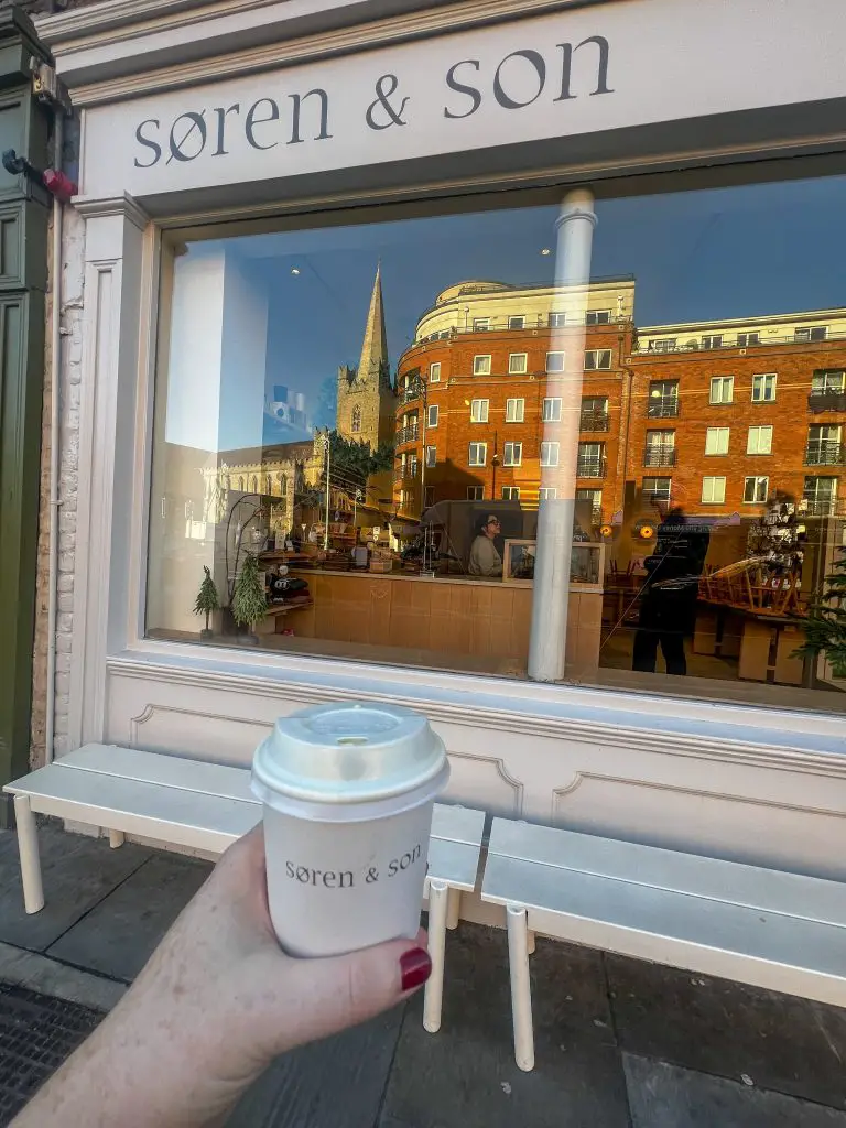 Holding a Soren and Son coffee cup in front of their coffee shop. 