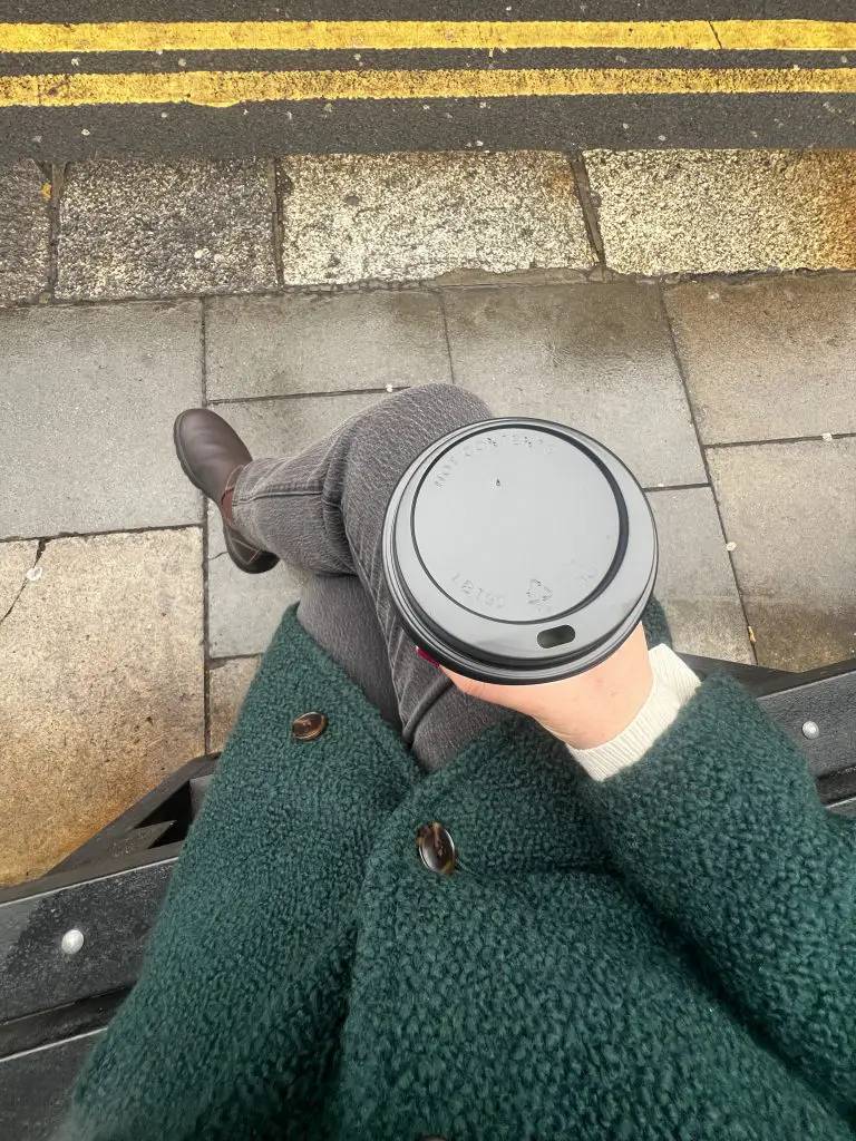 Holding a to go coffee container. 