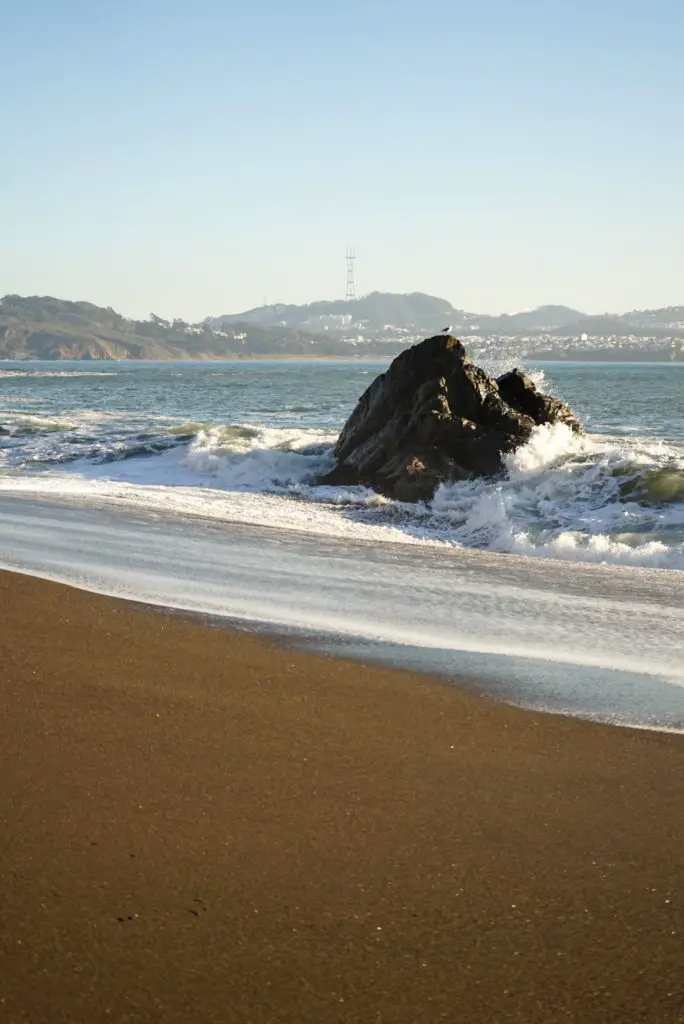 BBlack sand beach and a wave crashing against rock.