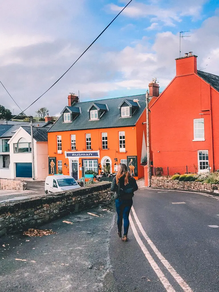 Woman walking down road towards orange pub.