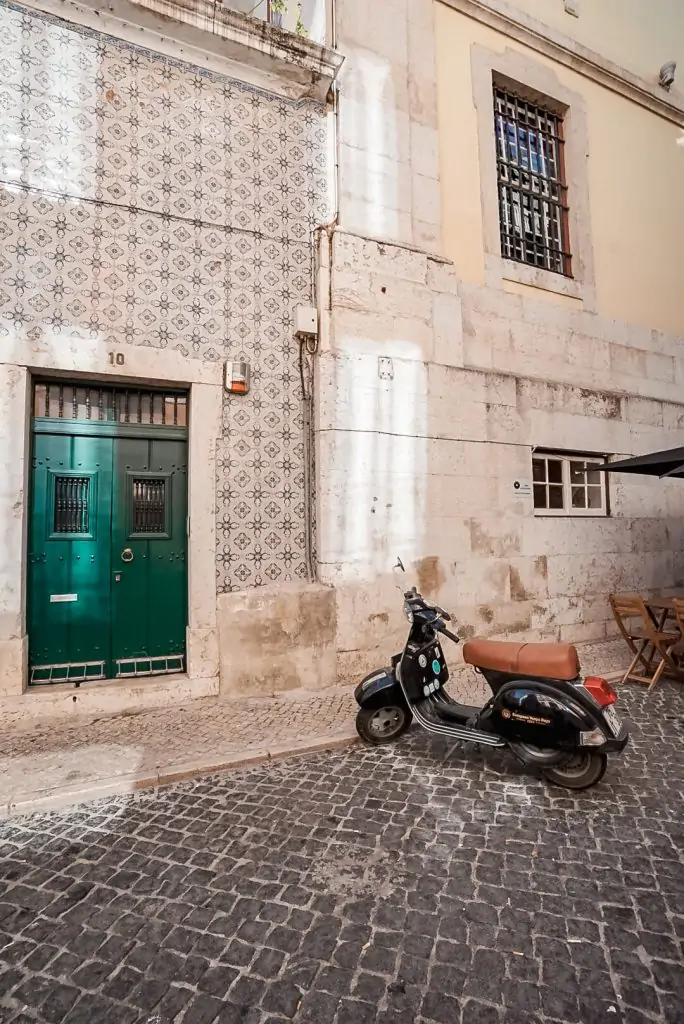 Lisbon street with a moped in front of a tiled building with a green door.
