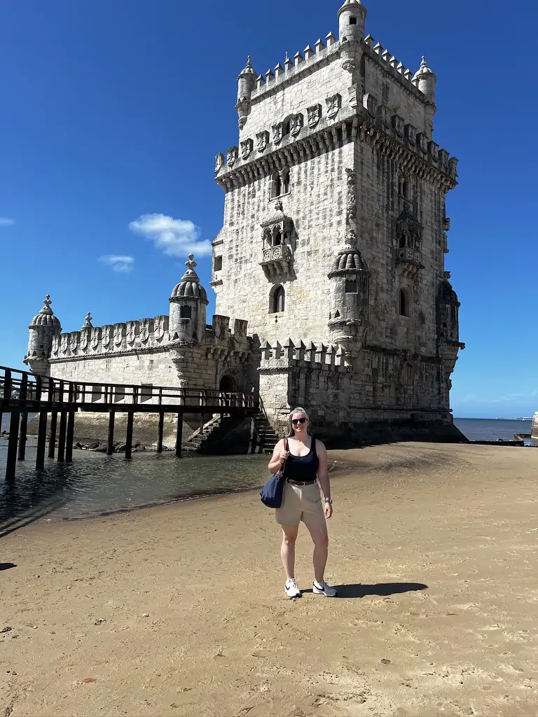 Wearing trouser shorts and blue tank top in front of Belém Tower in Lisbon, Portugal.