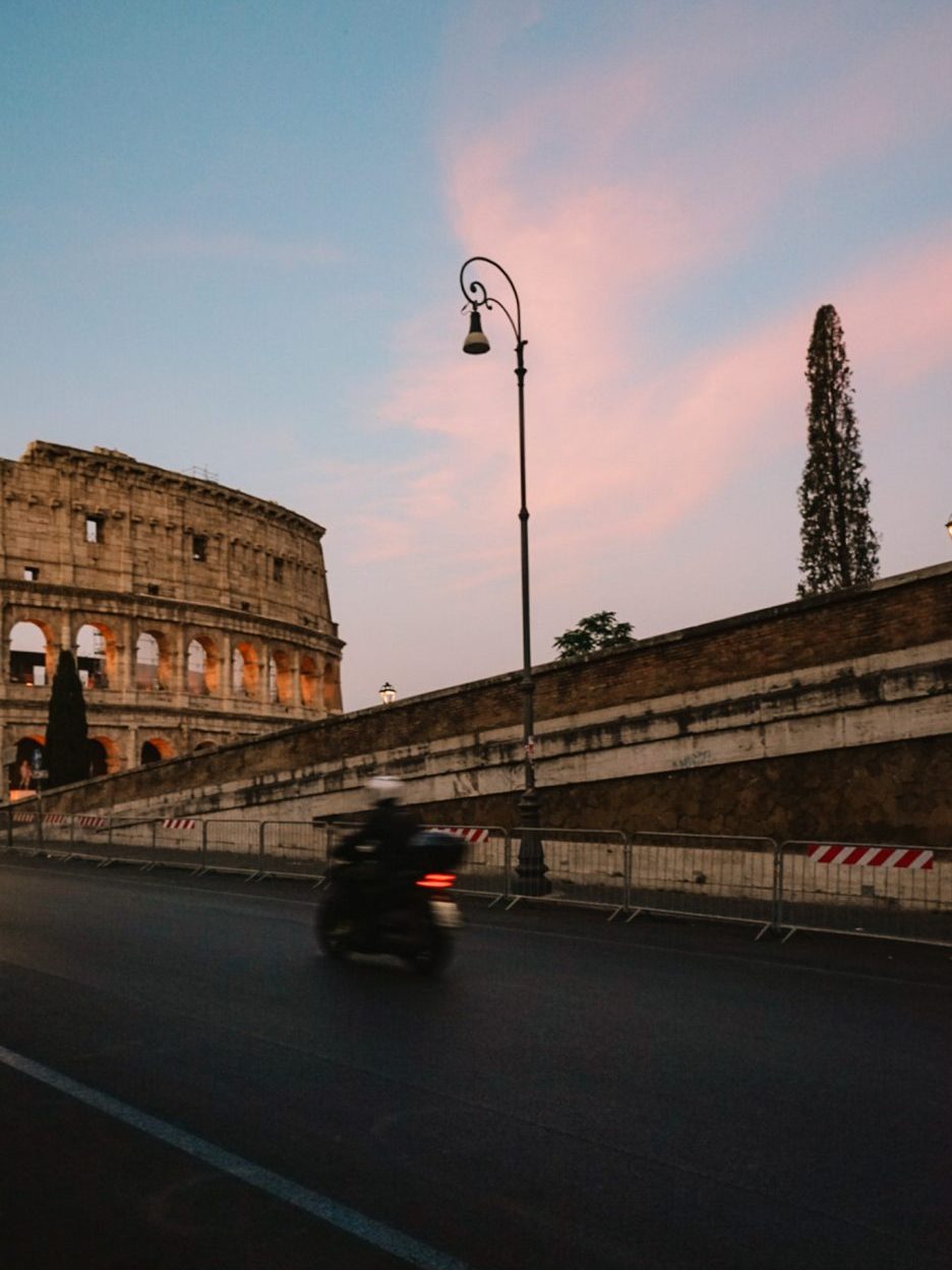 Moped driving on street in front of the Roman Colosseum in Rome, Italy.