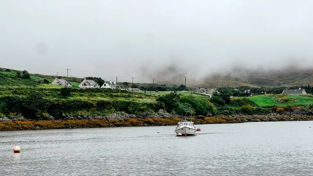 Boat in the water in front of green fields and homes in Donegal, Ireland.