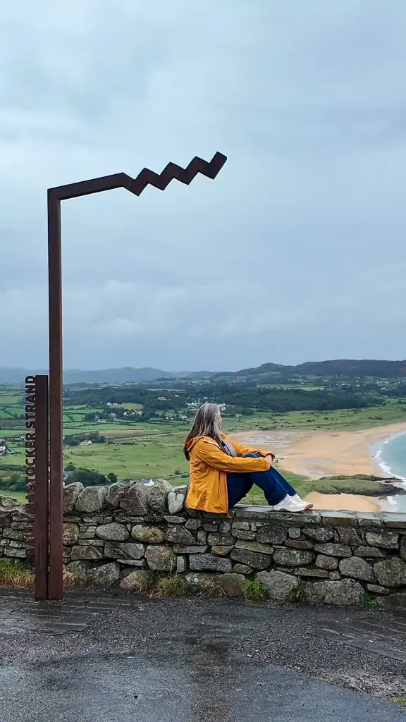 Sitting in front of Ballymastocker Strand Wild Atlantic Way sign in Donegal, Ireland.