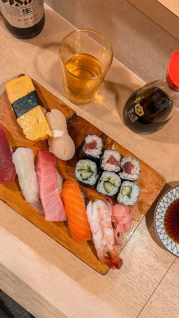 A plate of sushi, a glass of beer, and soy sauce.