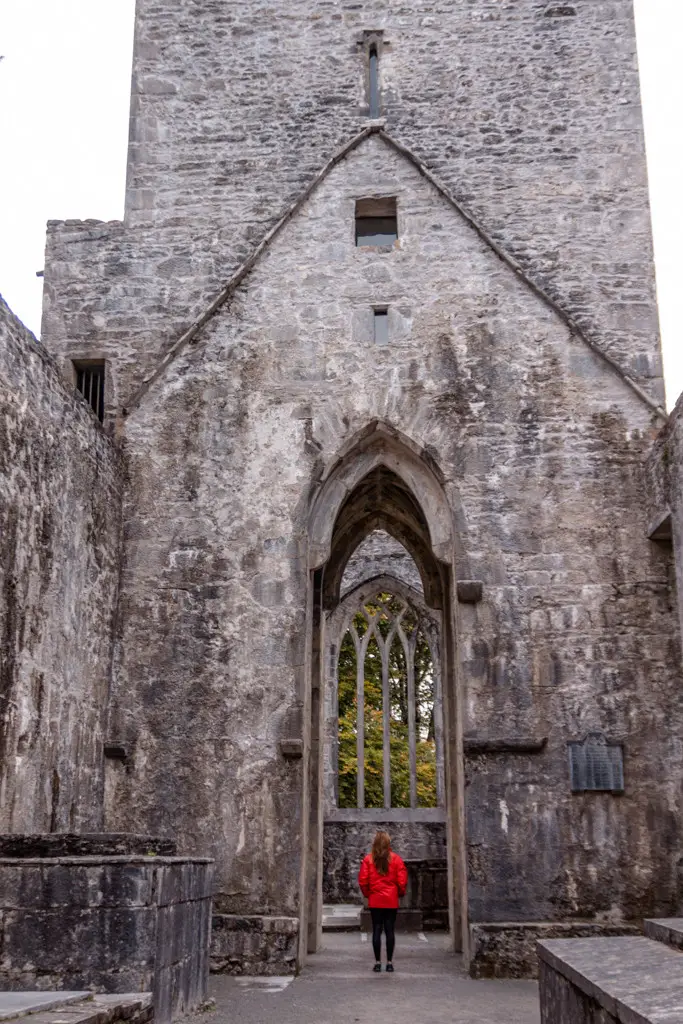 Katie wearing a red jacket standing in front of Muckross Abbey in Killarney National Park, Ireland.