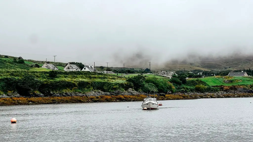 Boat floating in Donegal in front of green hills on a foggy day.