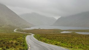 Windy road beside a lake leading into mountains on a rainy day in Doolough Valley Ireland. What it's like renting a car in Ireland.