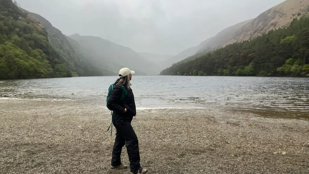 Katie standing in front of the Upper Lake in Glendalough on a rainy day wearing all black.