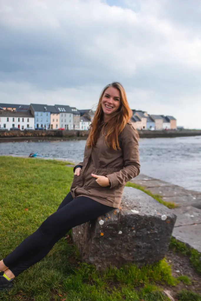 Katie sitting on a rock overlooking the colorful houses in Galway, Ireland.