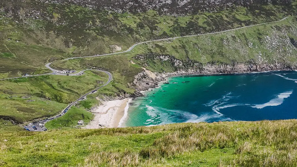 Keem beach on a sunny day as seen from above with a windy road leading to it.