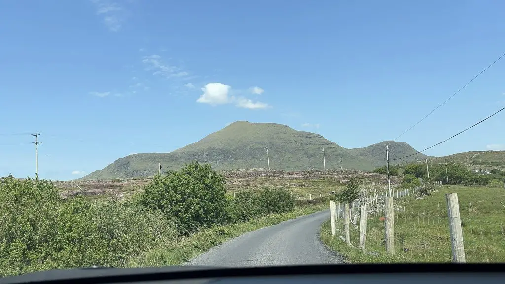 Windy road to beach in Connemara with a mountain in the distance on a sunny day.