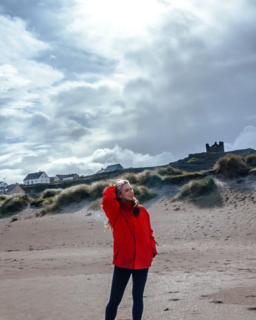 Katie standing on a white sand beach on a sunny day wearing a red jacket.